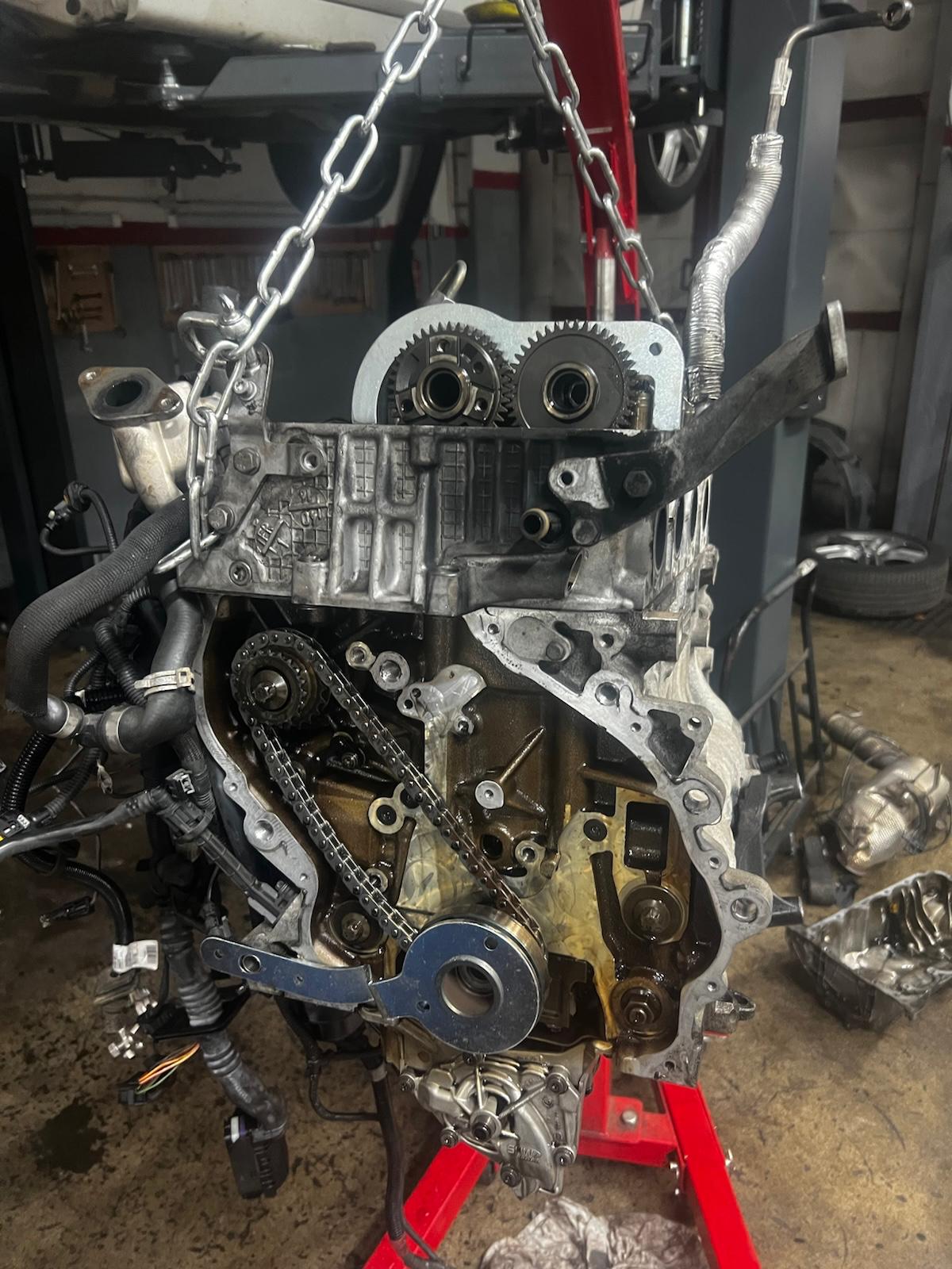 Motor zavěšený na jeřábu při opravě rozvodového řetězu